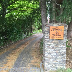 Un muro de piedra con un letrero que dice 'The Flying Trout Boutique Lodge' a lo largo de un camino rodeado de árboles.