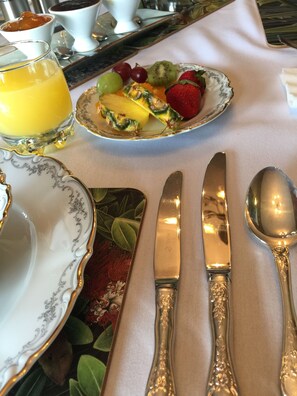 Desayuno servido con una fuente de fruta, un vaso de jugo de naranja y cubiertos sobre una mesa.