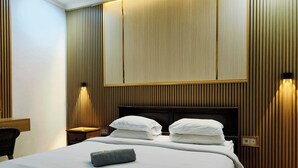 A hotel room with a large bed, two bedside tables, a wooden headboard, and wall-mounted lighting. - Ashana Hotel Uluwatu (Pecatu)