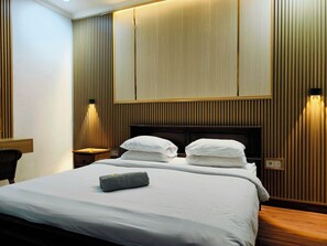 A hotel room with a large bed, two bedside tables, a wooden headboard, and wall-mounted lighting. - Ashana Hotel Uluwatu (Pecatu)