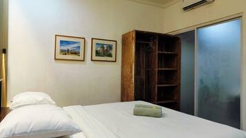 A hotel room with a bed, two pillows, a wooden wardrobe, and two framed pictures on the wall.