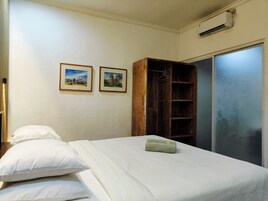Una habitación de hotel con una cama, dos almohadas, un armario de madera y dos cuadros en la pared.