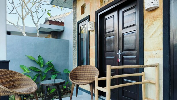 A modern exterior with a black door, a small round table, and two wicker chairs. - Ashana Hotel Uluwatu (Pecatu)