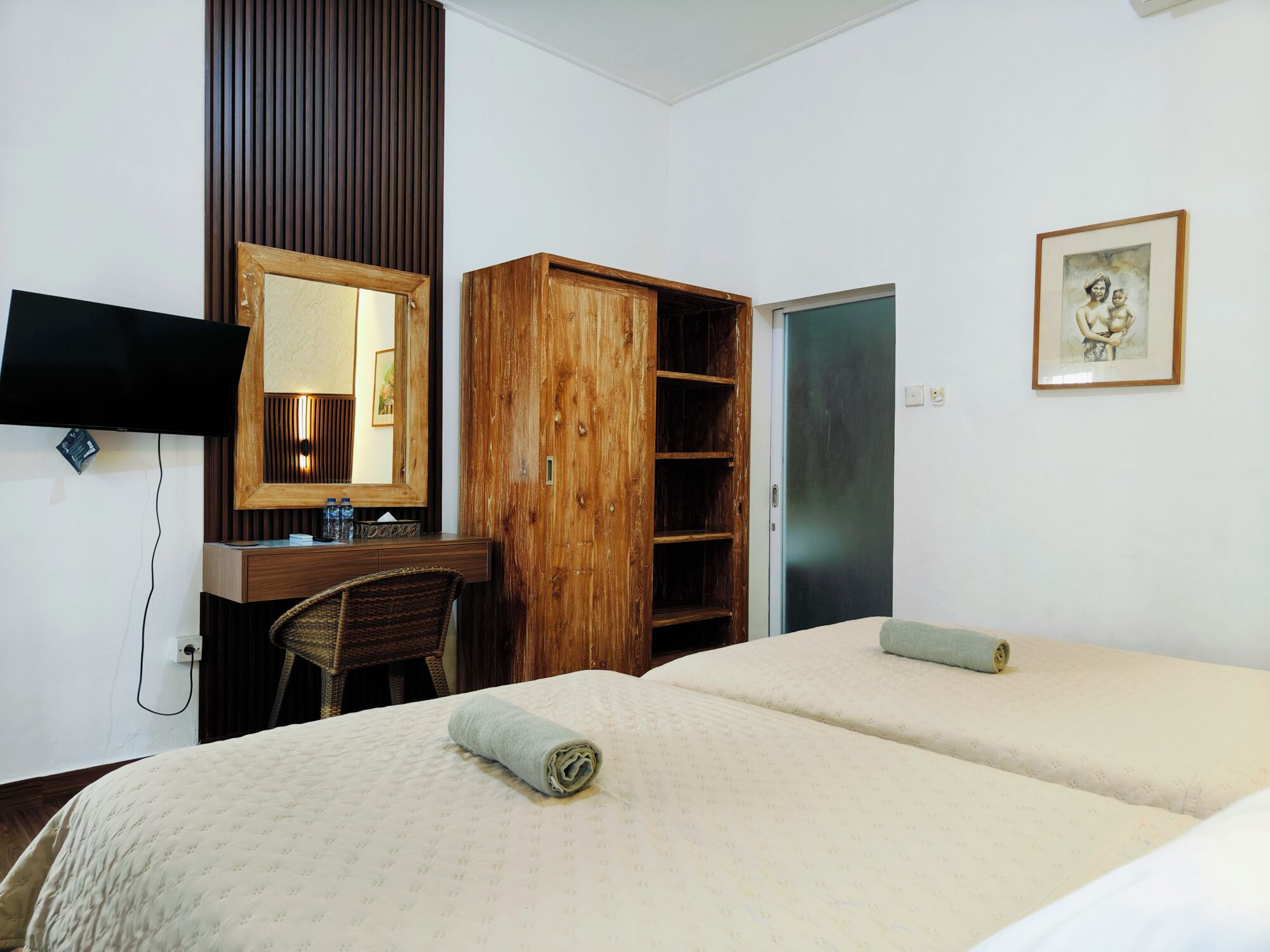 A hotel room with a desk, a wardrobe, a bed, a television, and a framed picture on the wall.