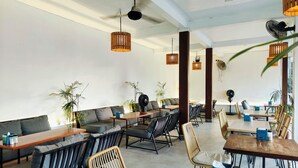 A modern restaurant with high ceilings, exposed beams, and a mix of seating options including tables and sofas. - Ashana Hotel Uluwatu (Pecatu)