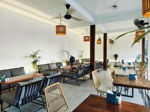 A modern restaurant with high ceilings, exposed beams, and a mix of seating options including tables and sofas. - Ashana Hotel Uluwatu (Pecatu)