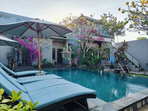 Ein Pool mit Liegestühlen, umgeben von blühenden Pflanzen und einem Gebäude mit einer Treppe.