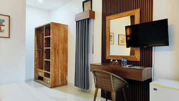 A hotel room with a wooden wardrobe, a desk with a chair, a television, and a small refrigerator.