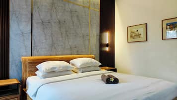 A hotel room with a large bed, a wooden headboard, a wall-mounted air conditioner, and two framed artworks on the wall.