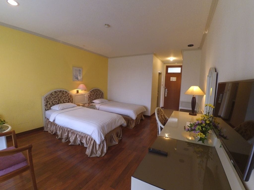 A hotel room with two beds, a desk with a TV, and a chair.