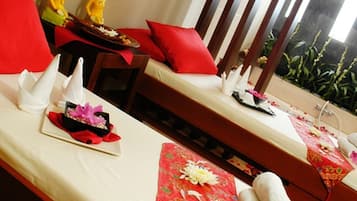Two beds with red pillows and white napkins, a small table with a decorative item, and a window overlooking lush greenery.