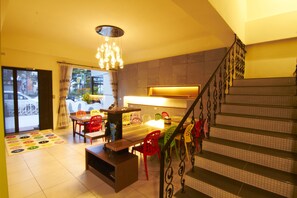 Un coin repas avec une table en bois et des chaises colorées, un escalier avec des rampes en métal et une vue sur la rue à travers une porte vitrée.