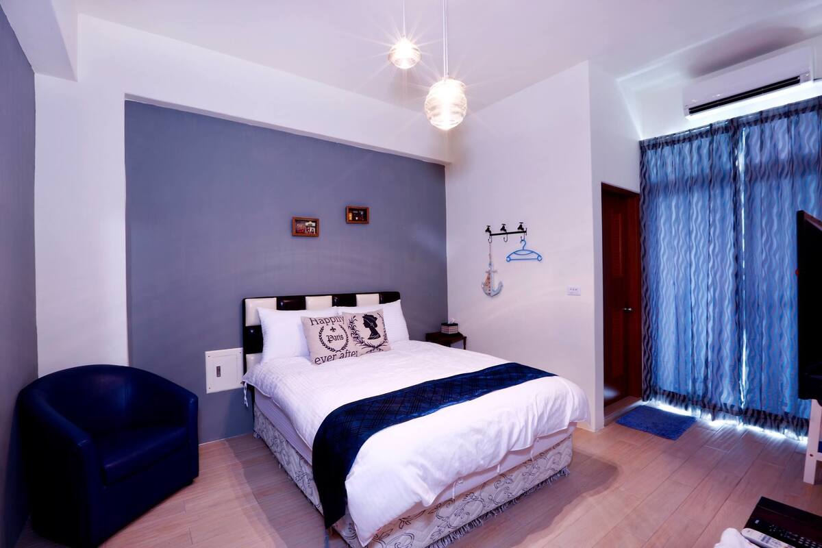 Une chambre à coucher avec un lit, une chaise bleue, une armoire et un luminaire suspendu.