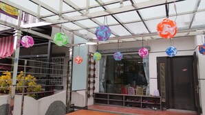 Zona exterior coberta amb decoracions esfèriques de colors penjant del sostre, una cadira de fusta i un aparador de sabates davant d'un edifici.