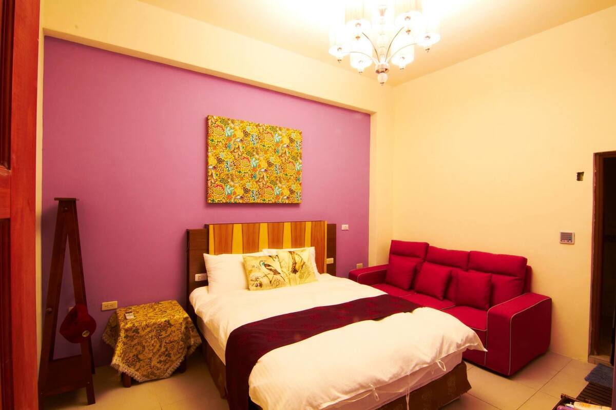 Une chambre à coucher avec un lit, un canapé rouge, un tableau au mur et un lustre.