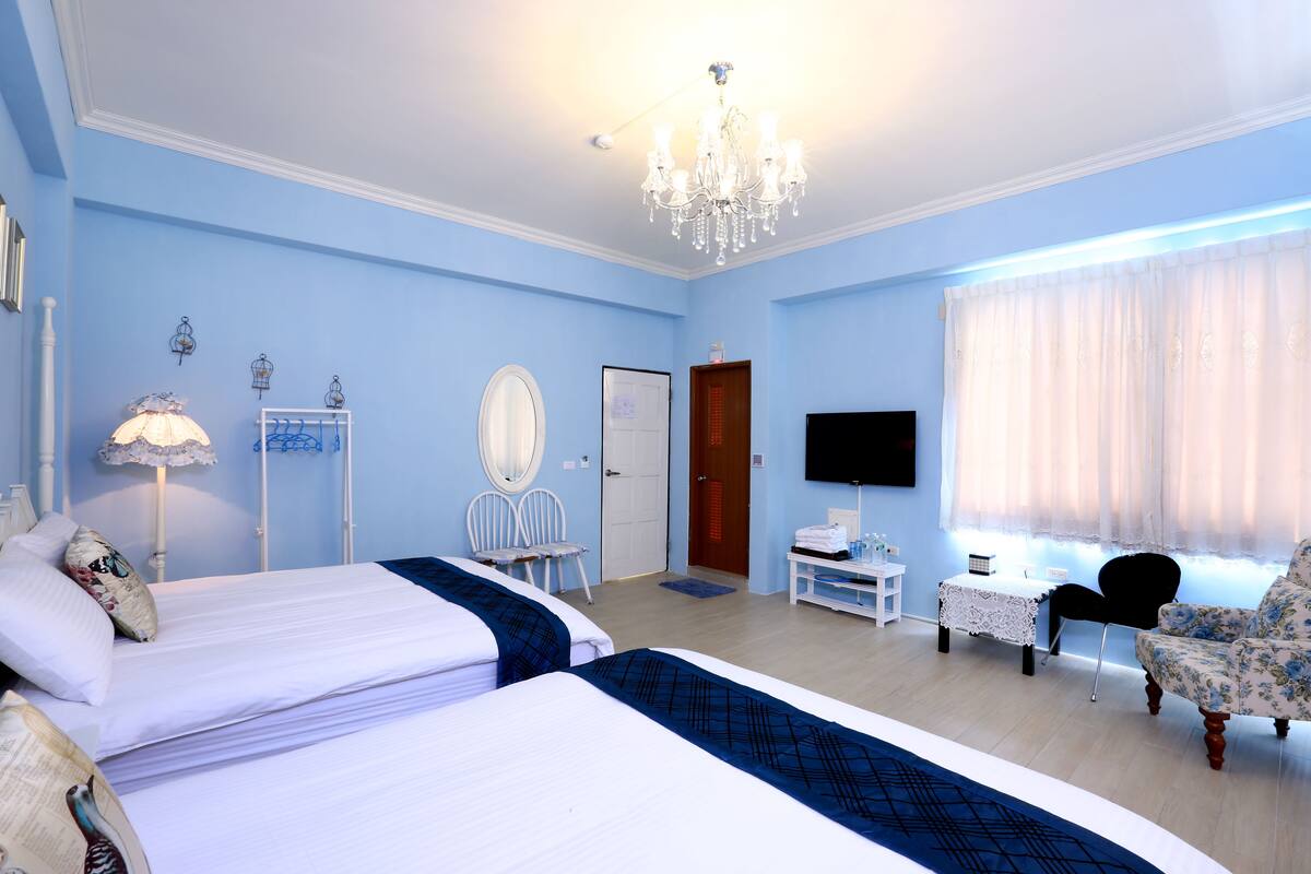 Une chambre d’hôtel avec deux lits, une télévision, un lustre et une fenêtre avec des rideaux.