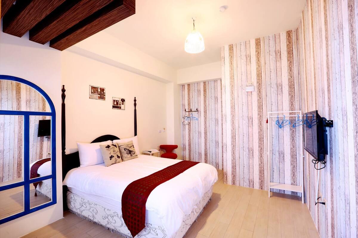 Une chambre avec un grand lit, un plafond en bois, un téléviseur fixé au mur et un papier peint à rayures.