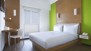 A modern hotel room with a large bed, a desk with a chair, a window, and a green accent wall. - Amaris Hotel Kupang (Kupang)