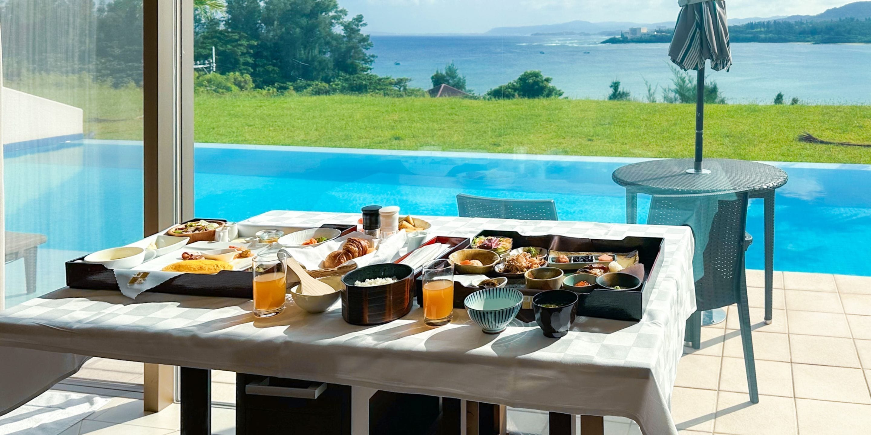Un tavolo da pranzo con una varietà di piatti e bevande, con vista su una piscina e un panorama mozzafiato sull'oceano e le colline.