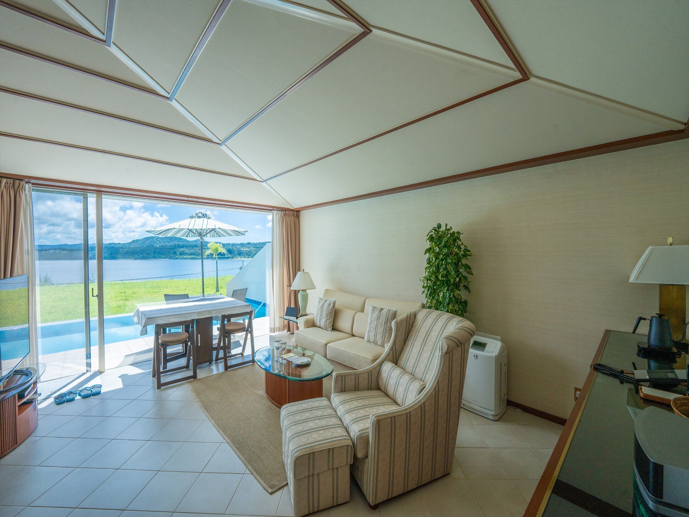 Un salón amplio con un sofá, una mesa de centro de vidrio y vistas a un lago.