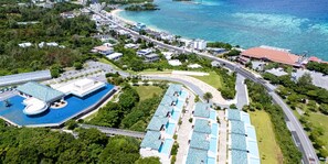 Eine Vogelperspektive zeigt einen Küstenort mit Pool, Strandvillen und einer sich an der Küste entlangschlängelnden Straße.