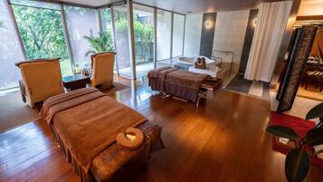 A modern spa room with two massage beds, a large window, and a bathtub.