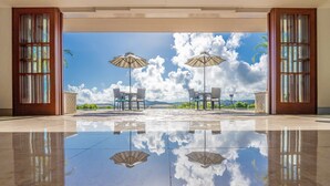 A spacious indoor area with a reflective floor, two umbrellas, and a view of the sky and clouds through large windows. - Oriental Hills Okinawa (Onna)