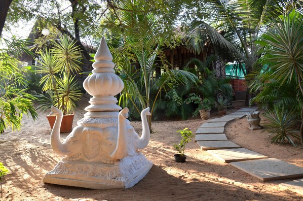 A garden with a white elephant statue, potted plants, and a stone pathway. - Little India Beach Cottages (Calangute)