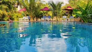 Una piscina cristalina rodeada de sillones de descanso y sombrillas, con abundante vegetación de fondo.
