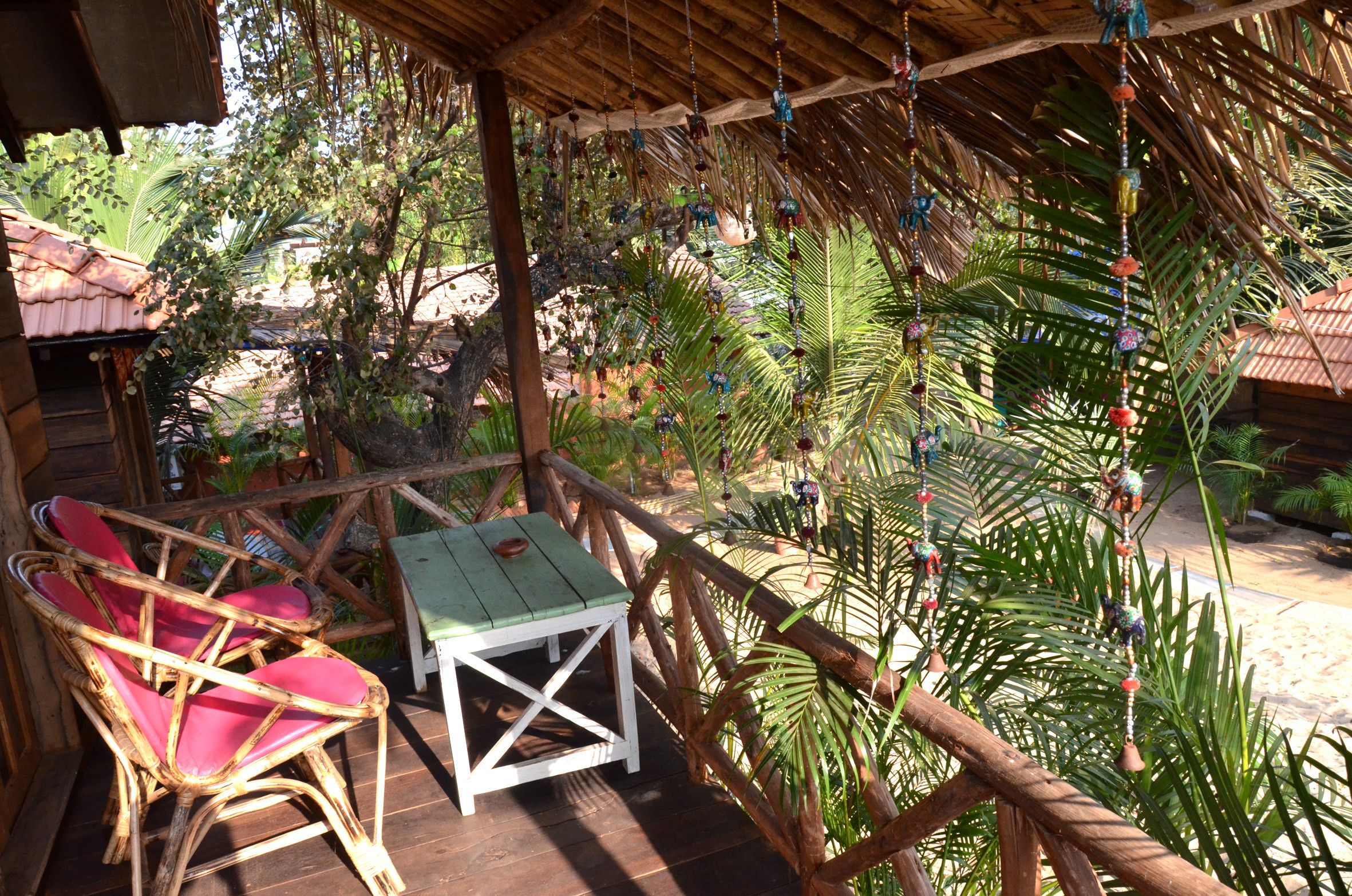 Una terraza de madera con sillas de mimbre y una mesa, rodeada de abundante vegetación y un techo de paja.