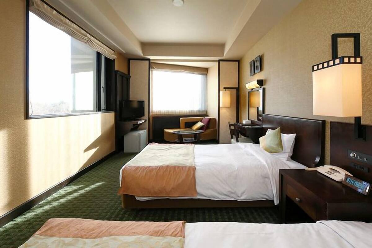 A hotel room with two beds, a TV, a desk, a chair, and a window.