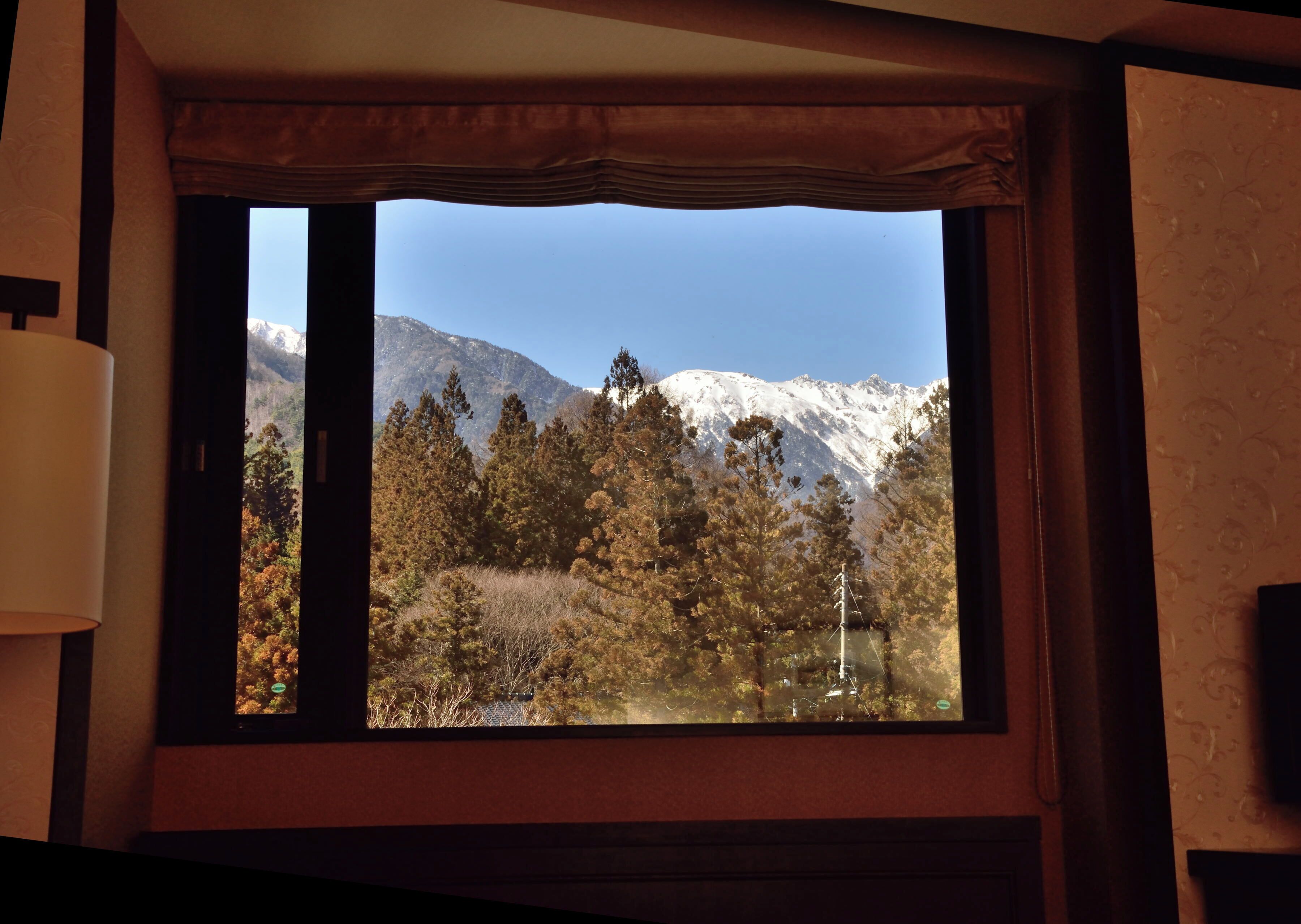 Una ventana con vistas a un paisaje montañoso, una lámpara y un muro con diseño.