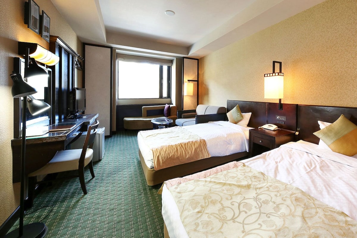 A hotel room with two beds, a desk, a chair, a telephone, and a window.