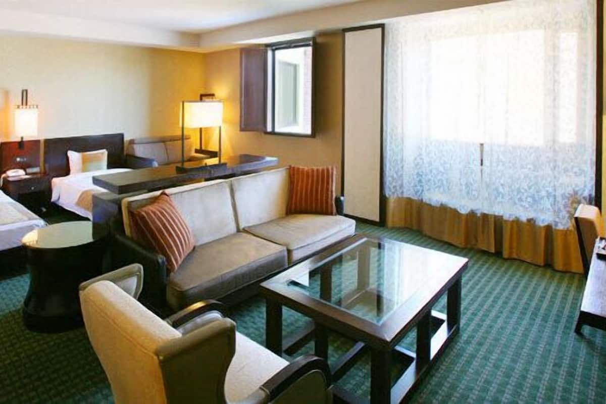 A hotel room with two beds, a sofa, a glass coffee table, and a desk with a lamp.