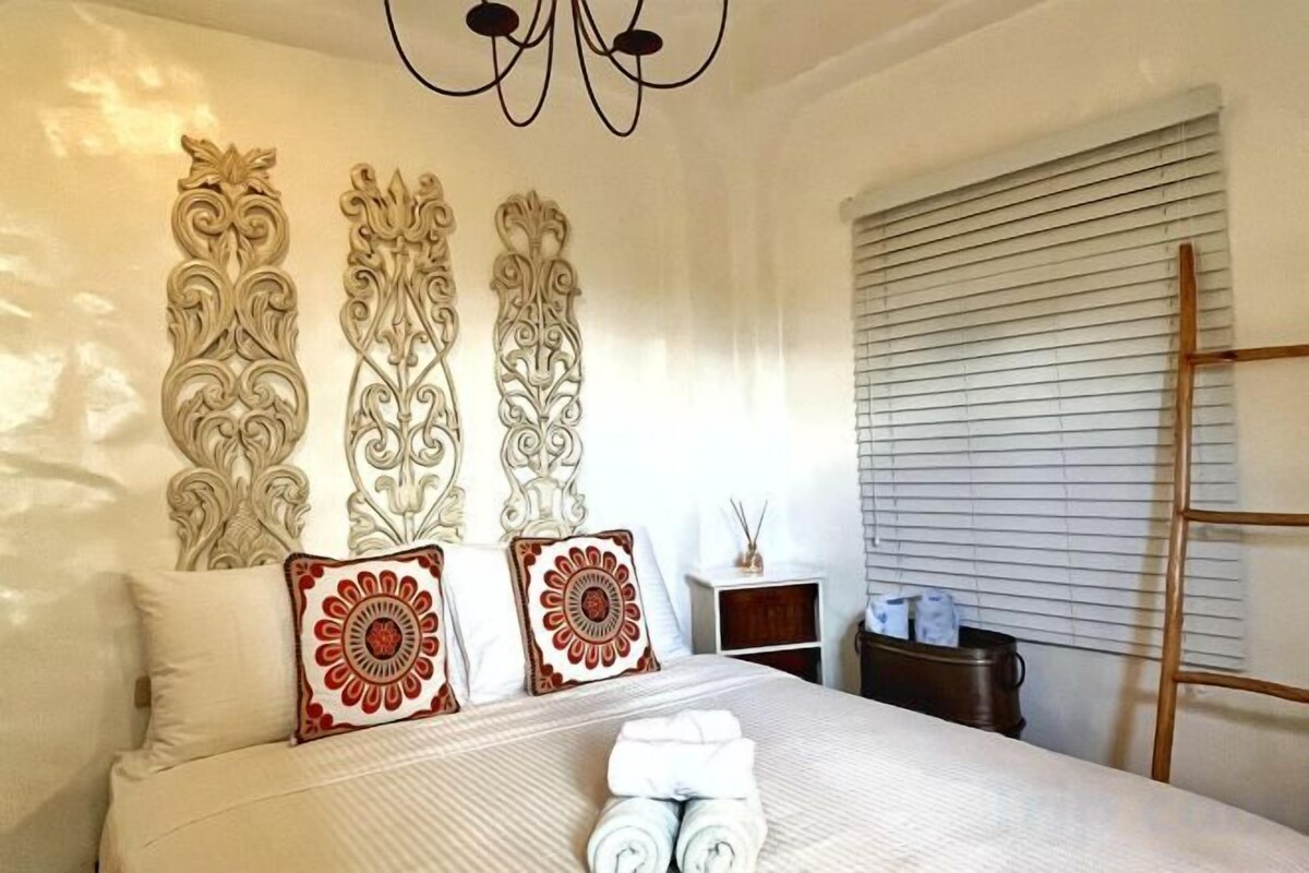 Een hotelkamer met een bed, decoratieve wandpanelen, een nachtkastje met een lamp en een raam met zonwering.