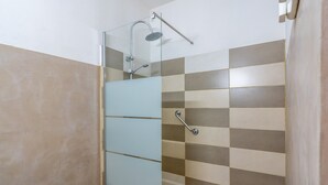 A shower with a glass door, a handheld showerhead, and a handheld showerhead attachment.