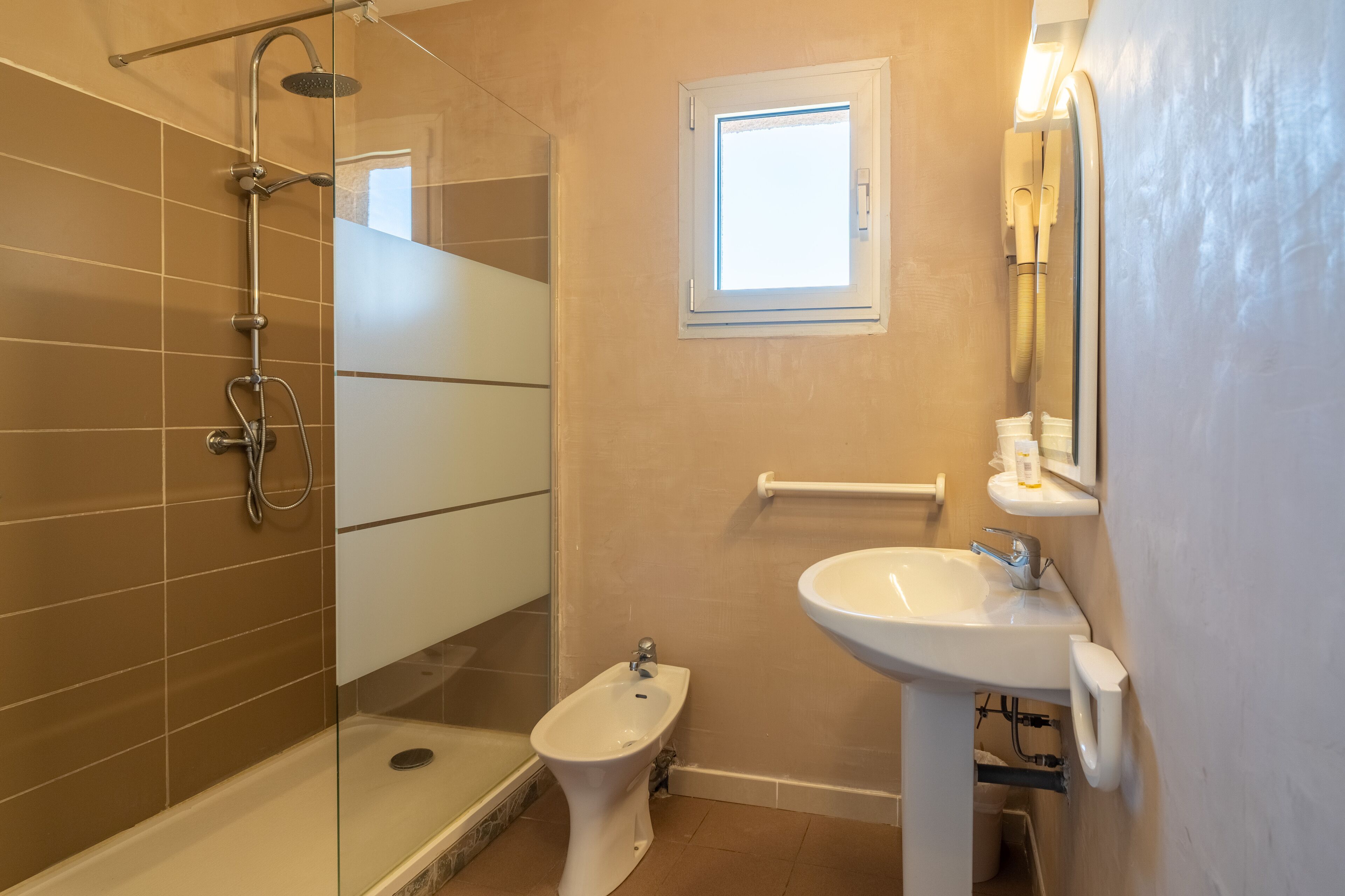Een badkamer met een glazen douchecabine, een bidet, een wastafel en een raam.
