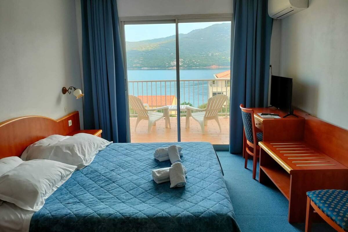 Une chambre d’hôtel avec un lit, un bureau, une chaise et une vue sur la mer et les montagnes.