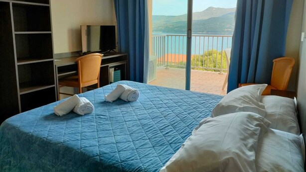 A hotel room with a bed, a desk, a TV, and a balcony with a view of the mountains.