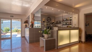 A hotel lobby with a reception desk, a clock, and a view of the outdoors.