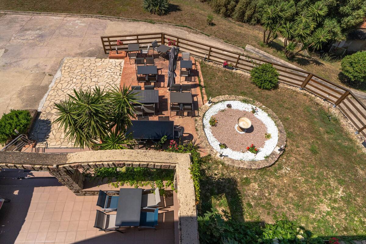 Une terrasse extérieure dotée de plusieurs tables et chaises, entourée d’un mur de pierre et d’une clôture en bois.