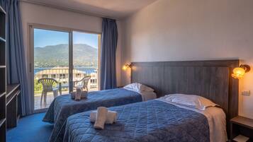 A hotel room with two beds, a balcony with a view of the sea and mountains, and a wooden headboard.