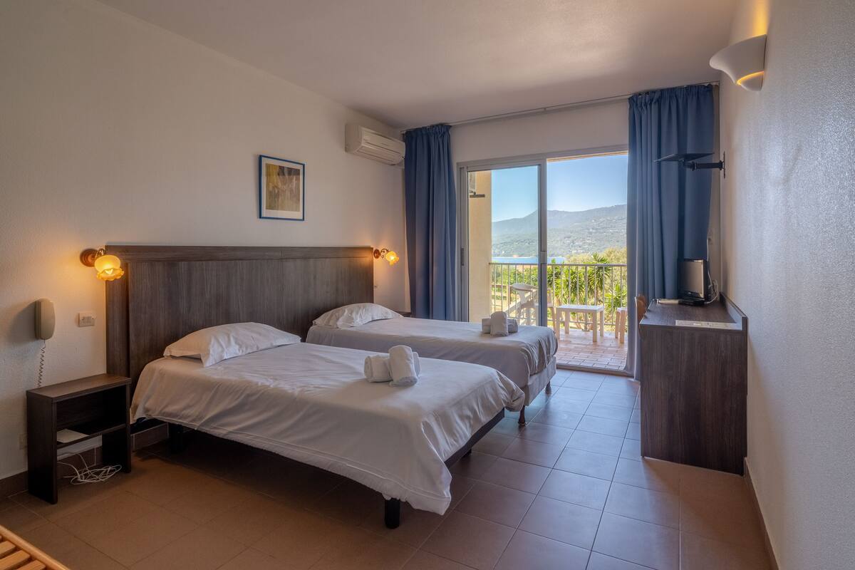 Une chambre d’hôtel avec deux lits, un bureau, une chaise et un balcon avec vue.