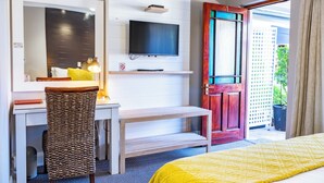 Une chambre d’hôtel comprenant un lit, un bureau avec une chaise, une télévision et une porte donnant sur un espace extérieur.