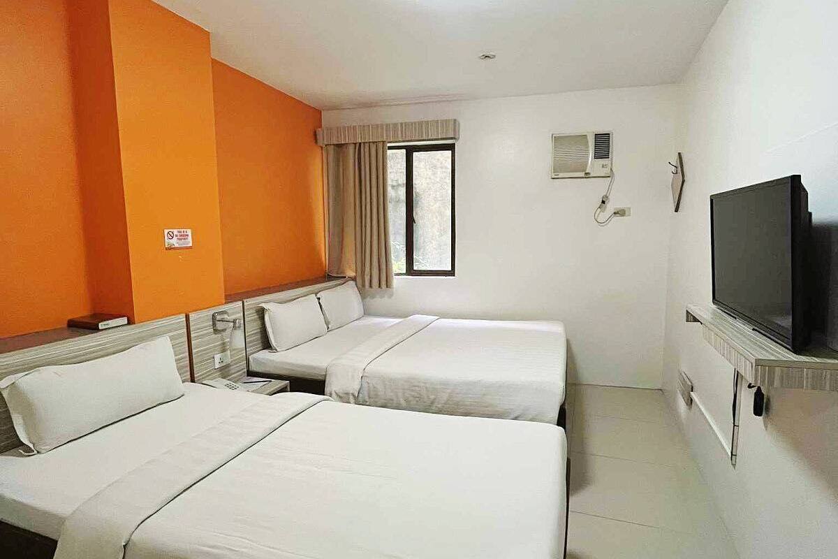 Quarto de hotel com duas camas, televisão, aparelho de ar condicionado e janela com cortinas.