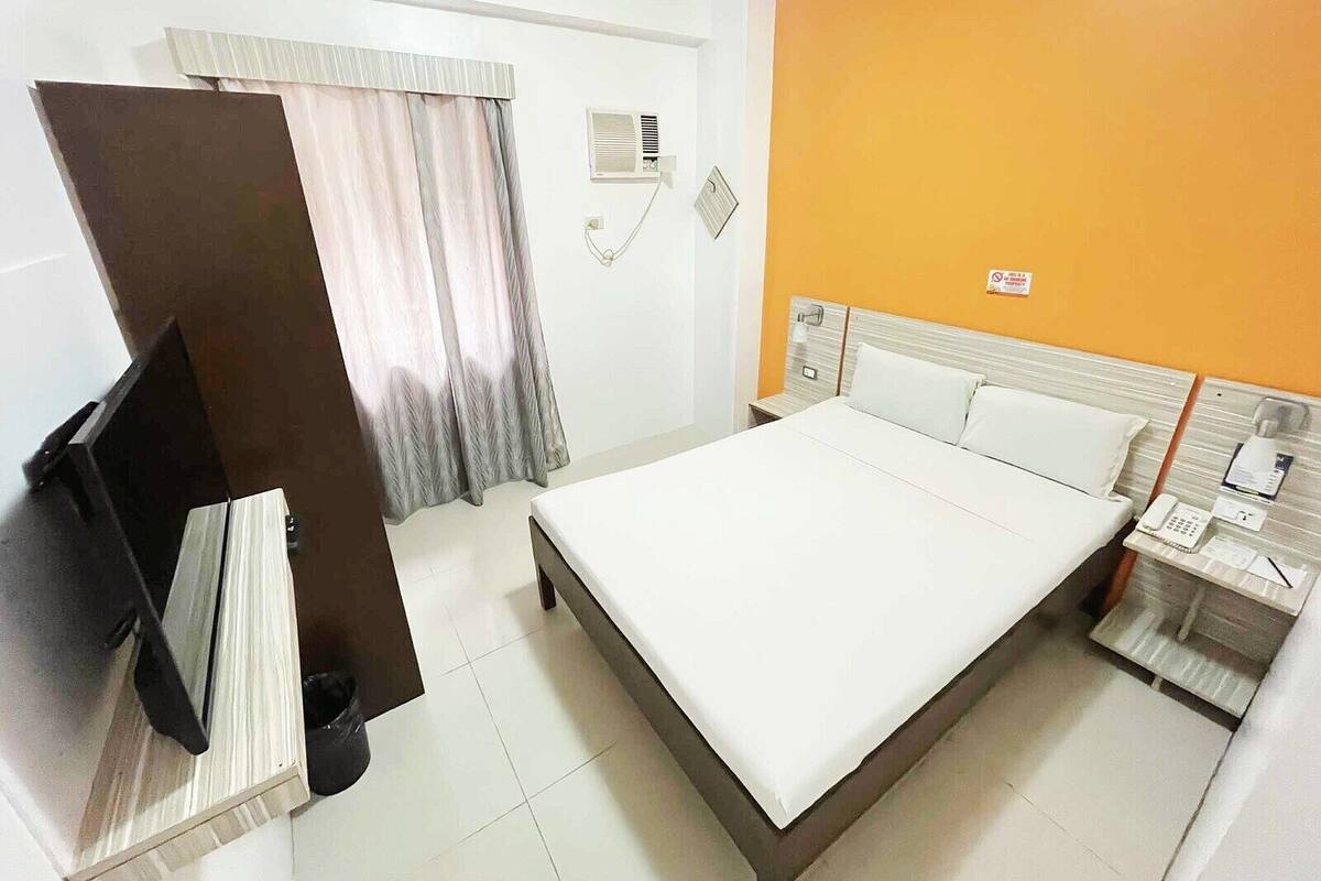 Quarto de hotel com cama, escrivaninha, telefone e televisão.