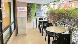 A balcony with tables and chairs, a sign for Travelbee Business Inn, and a view of the street with buildings and greenery.
