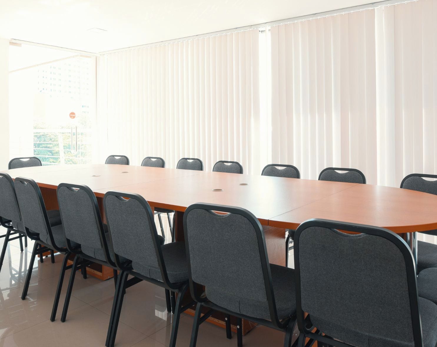 A conference room with a long table and chairs, large windows with blinds, and a whiteboard.