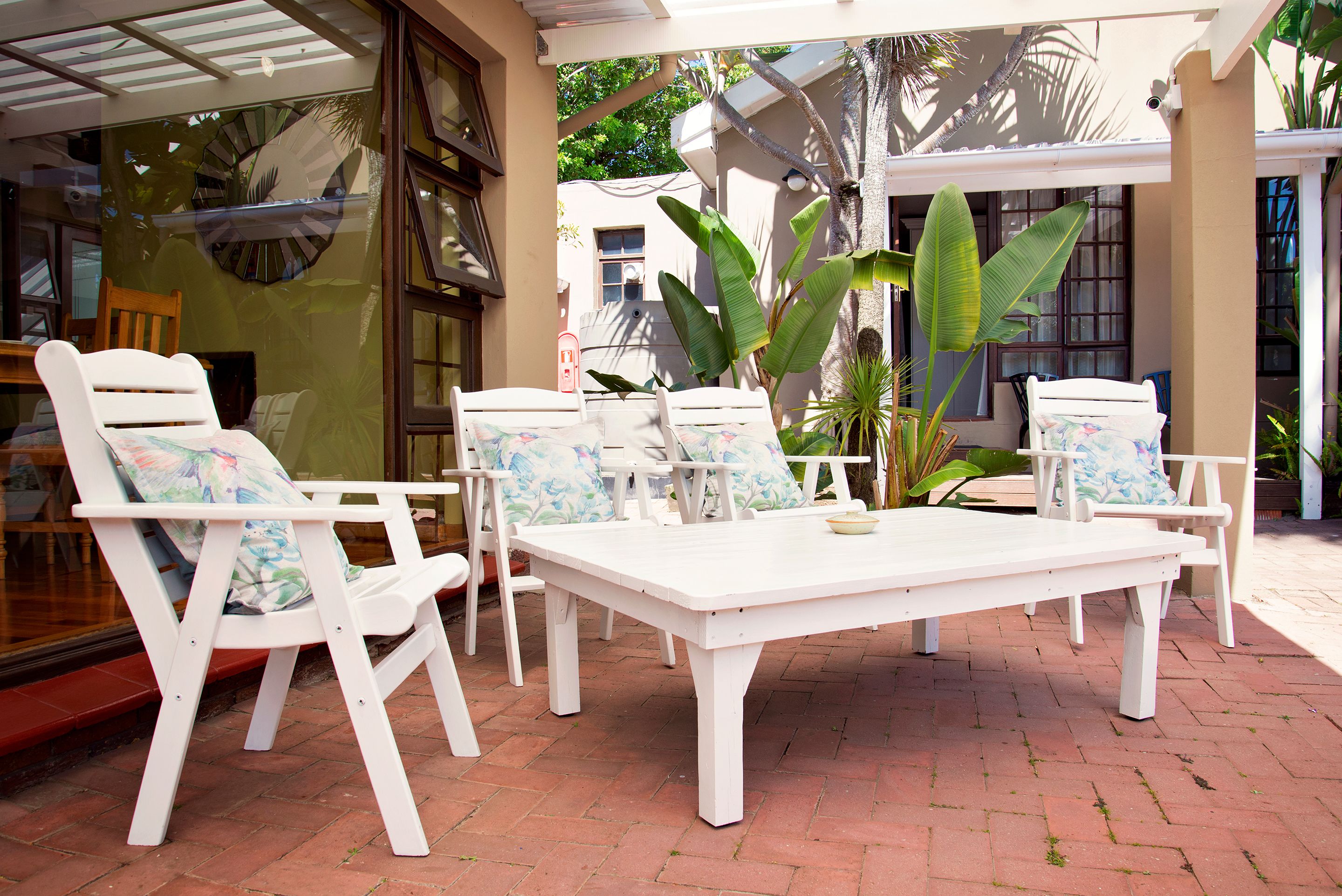 A patio area with a white table and chairs, surrounded by potted plants and a glass door.