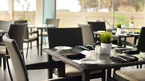 A restaurant with wicker furniture, white plates, and a potted plant on the table. - The Beach Apartments (Negombo)